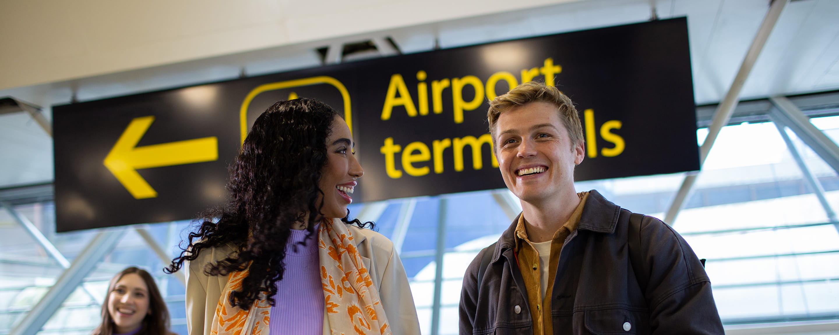 Two people smiling in front of an airport sign