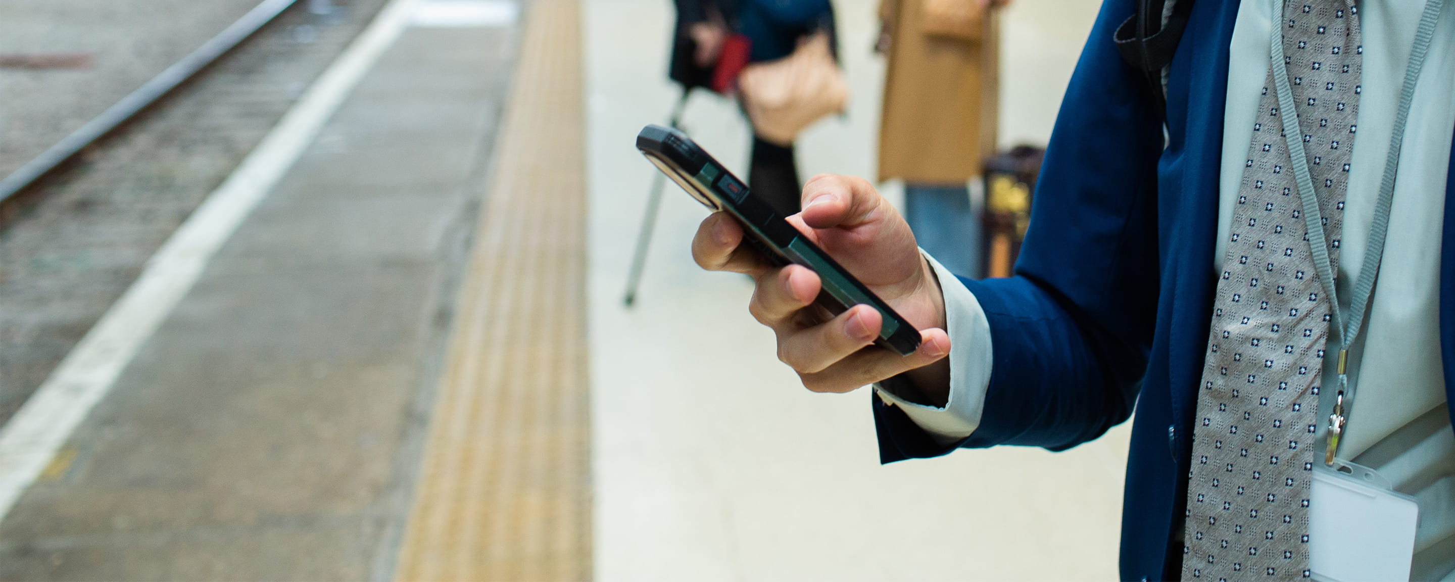 A man looking at his phone on a train platform with two people in the background