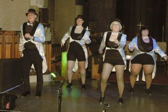 Three women and a man perform tap dancing on stage